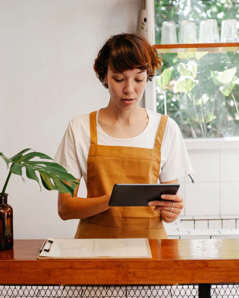 A bakery owner in her apron at the counter, checking feedback on a tablet